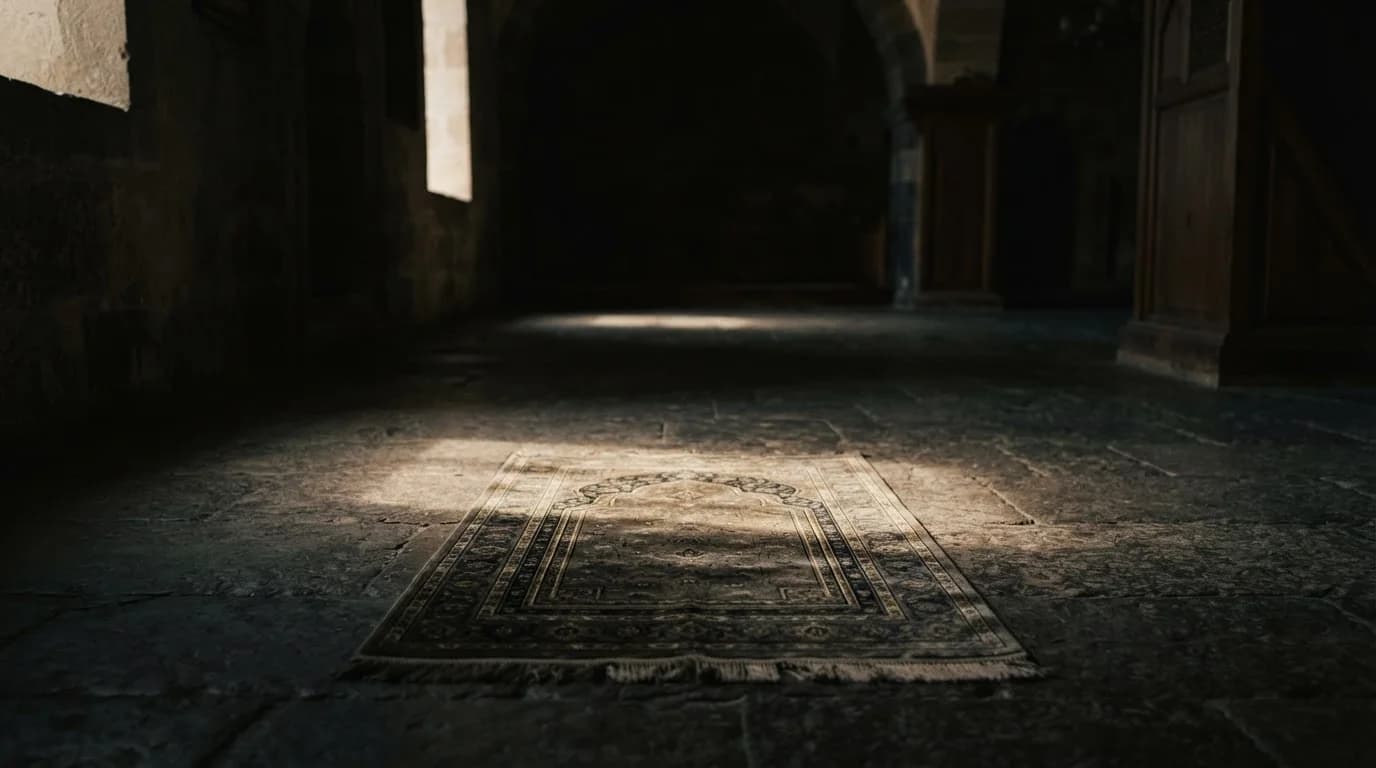 A prayer mat laid on a stone floor in a dim, quiet hall, lit by a soft shaft of daylight